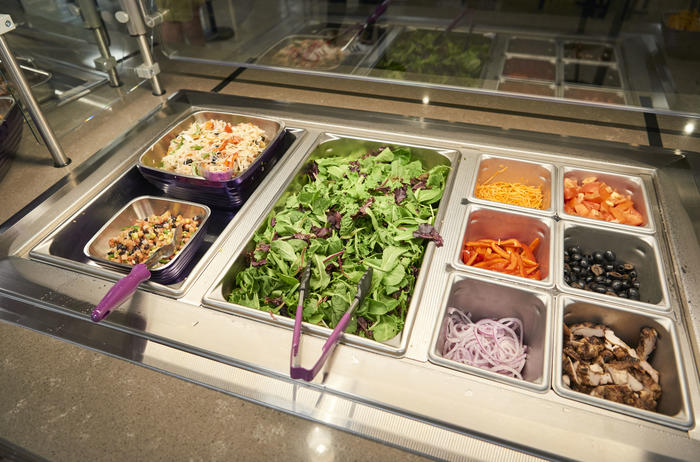 Salad bar featuring a spring mix salad and a variety of toppings